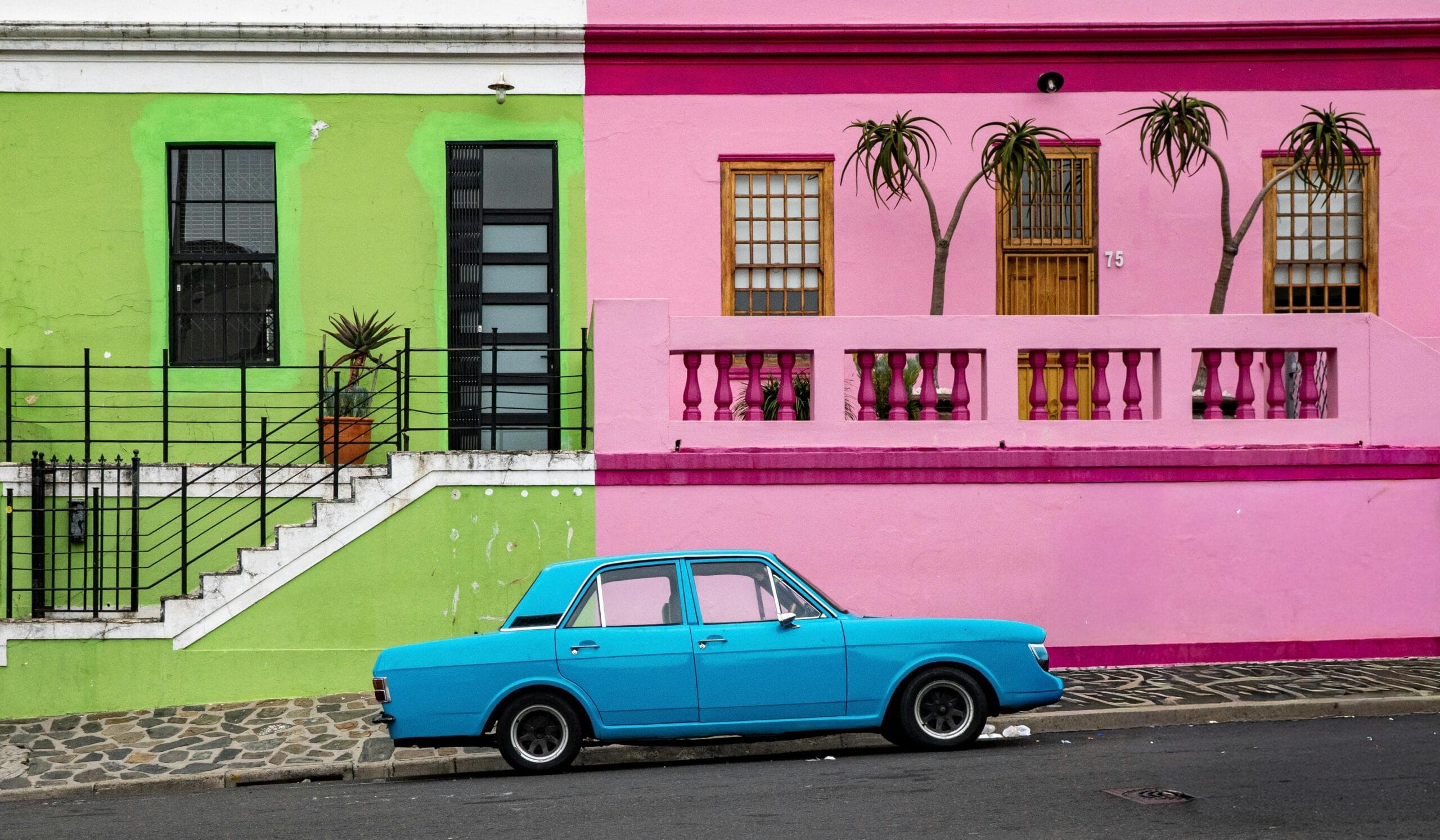 Vibrant pink and green houses with a classic blue car in Bo-Kaap, Cape Town.