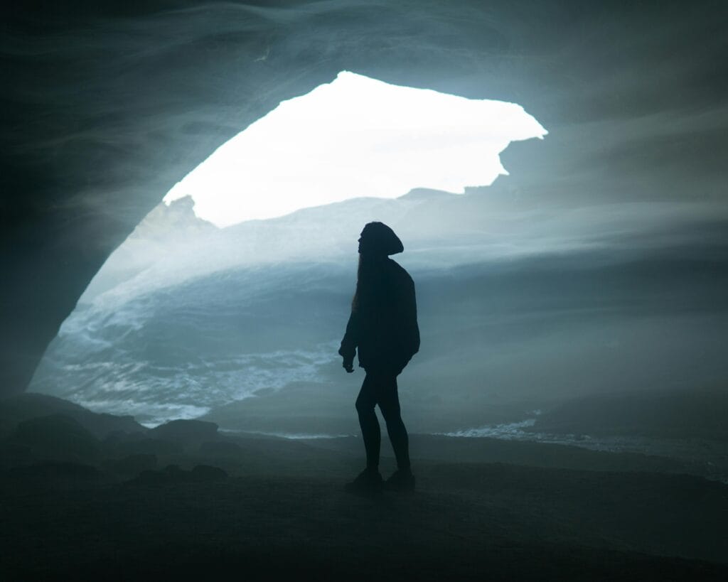 A silhouette of a woman standing inside a mysterious cave, evoking a sense of adventure.